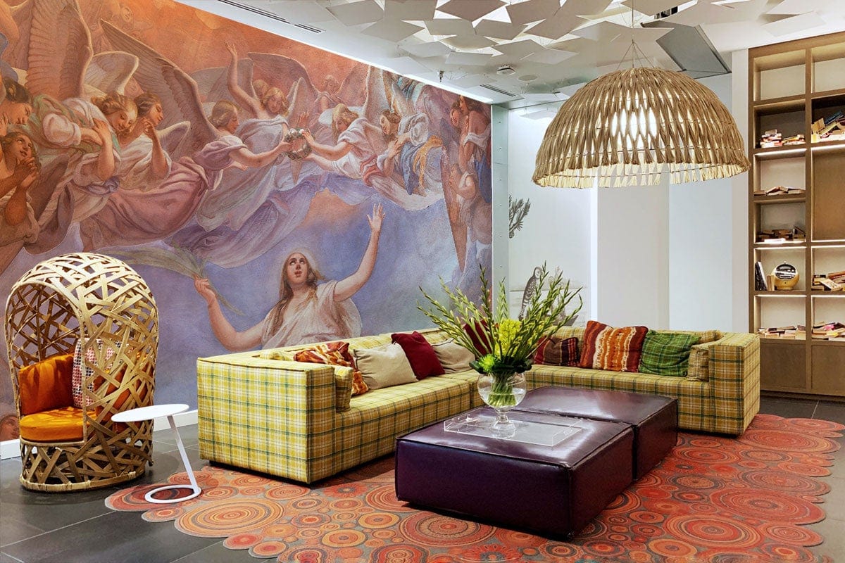 Angel-themed Celestial Renaissance mural wallpaper enhances room with plaid sofas, luxe rug, statement light fixture.