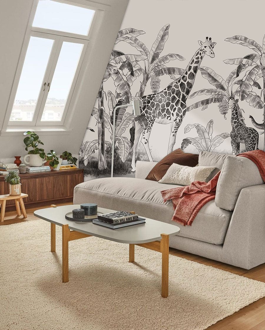 Vintage Safari Jungle Mural Wallpaper featuring giraffes, monochrome style, with grey sofa, wooden flooring.