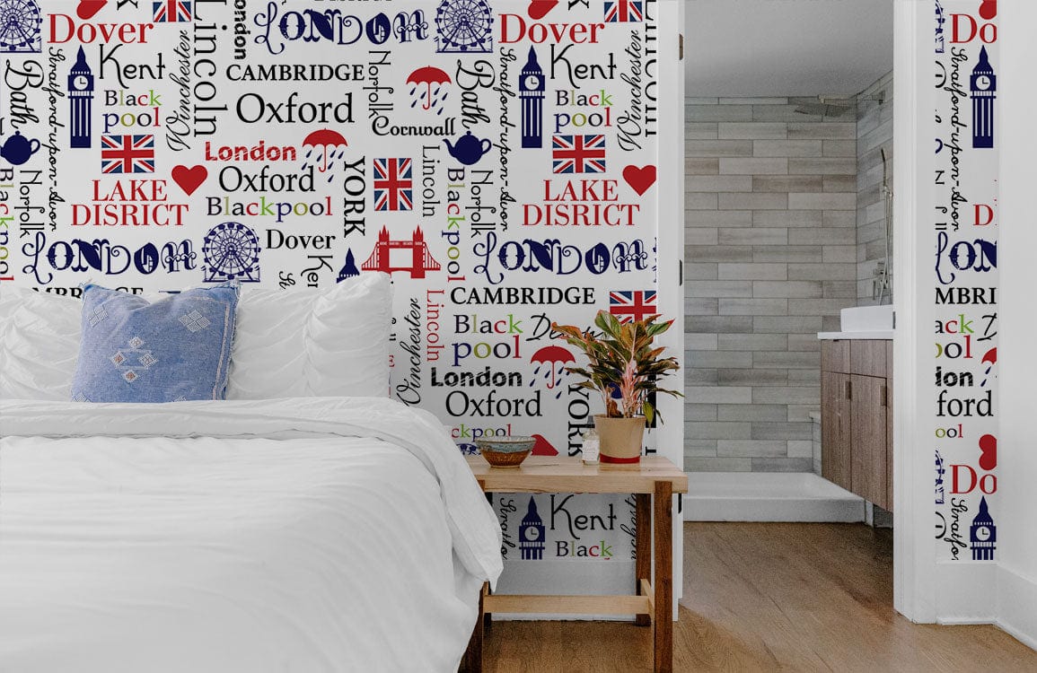 British Iconography wallpaper in bedroom with blue cushion, wooden flooring, and bathroom glimpse on right.
