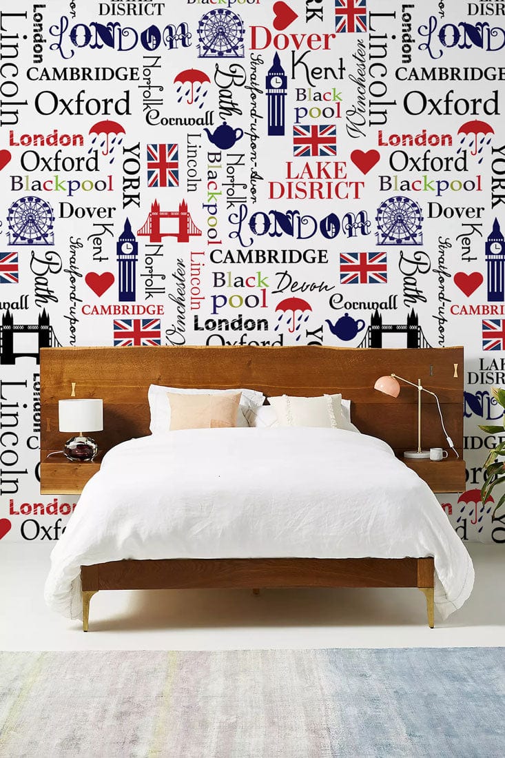 British iconography wallpaper in bedroom with white bed, wooden headboard, white and pastel rug flooring.