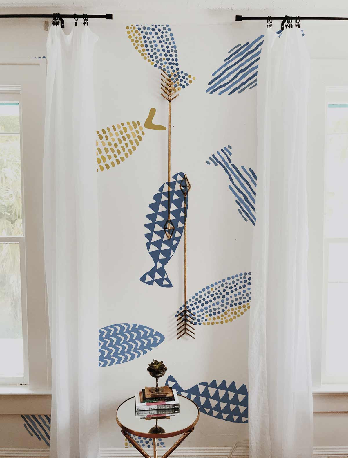 Blue and Gold Geometric Fish wallpaper in nautical style with white curtains and decorative table.