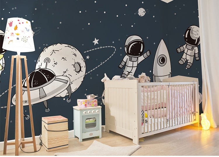 Navy space-themed children's wallpaper with astronauts, rockets; nursery crib, play kitchen, and wooden flooring.