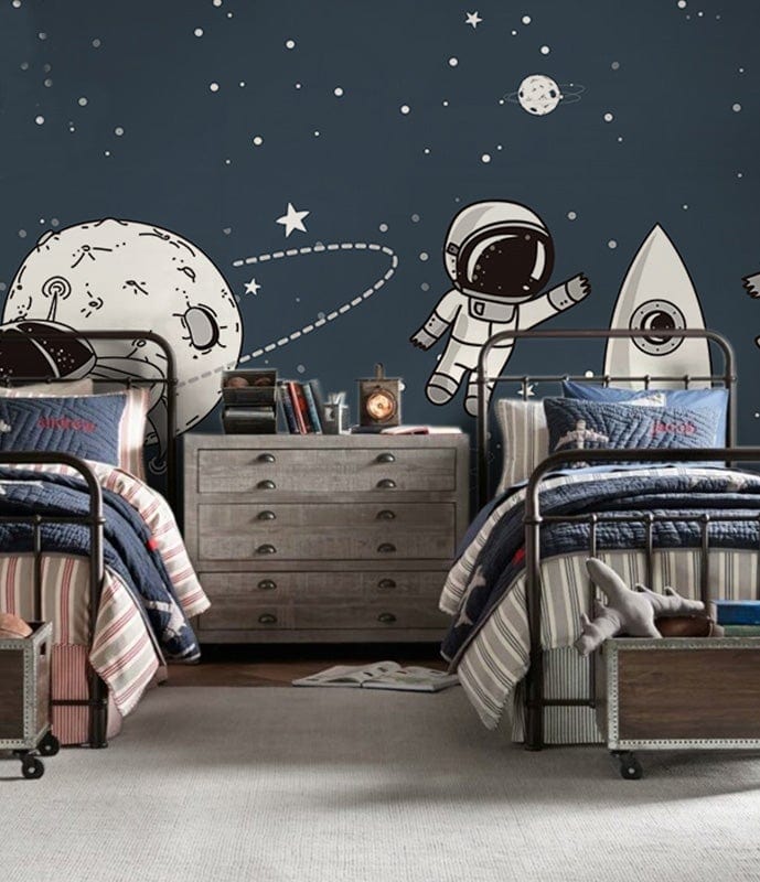 Children's room with navy space-themed wallpaper, featuring astronauts and rockets, metal beds, grey dresser.
