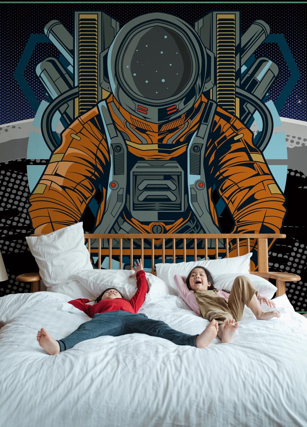 Retro Astronaut Space Adventure Mural Wallpaper in orange and blue behind a cosy white bed with pillows.