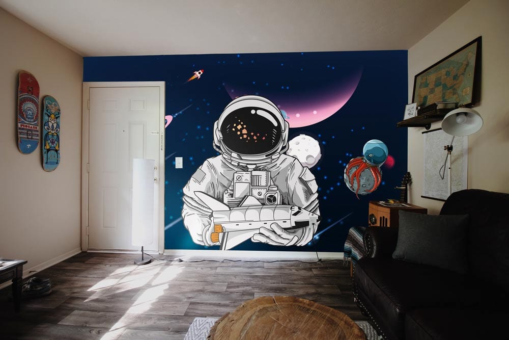 Navy blue space-themed mural wallpaper with astronauts, rockets; dark sofa; wooden flooring; living room.