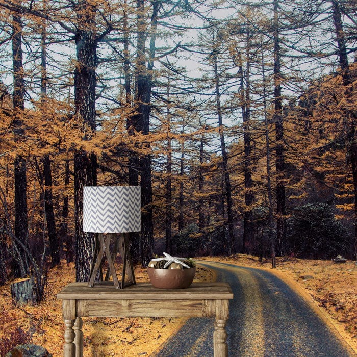 Rustic room with Autumn Forest Path Wallpaper, wooden table, lamp, and golden hues in nature theme.