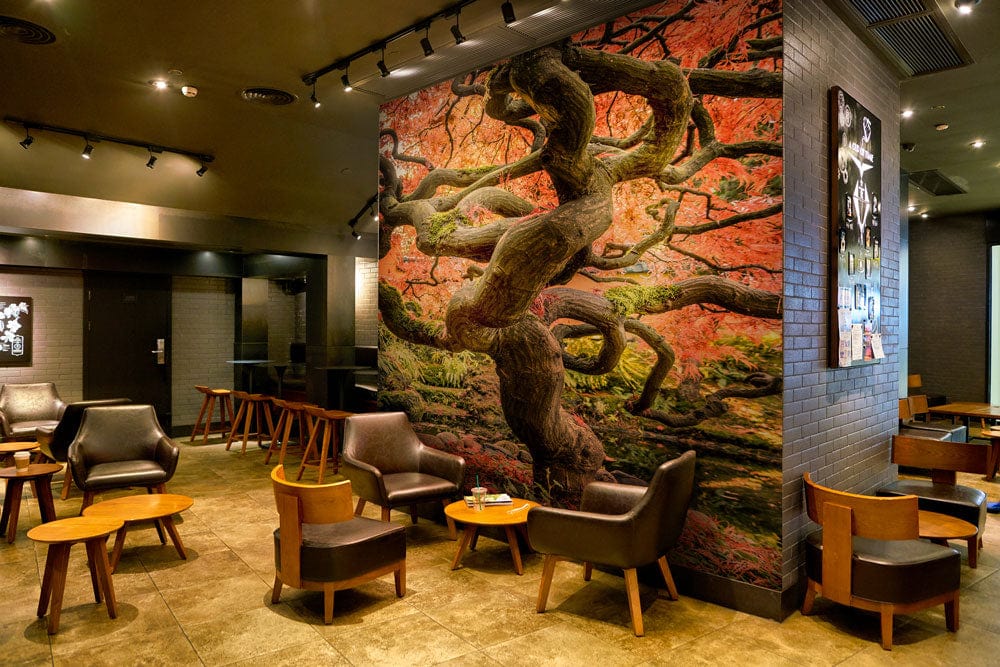 Cafe interior featuring Vibrant Autumn Japanese Maple Tree mural wallpaper with brown leather chairs and wooden tables.
