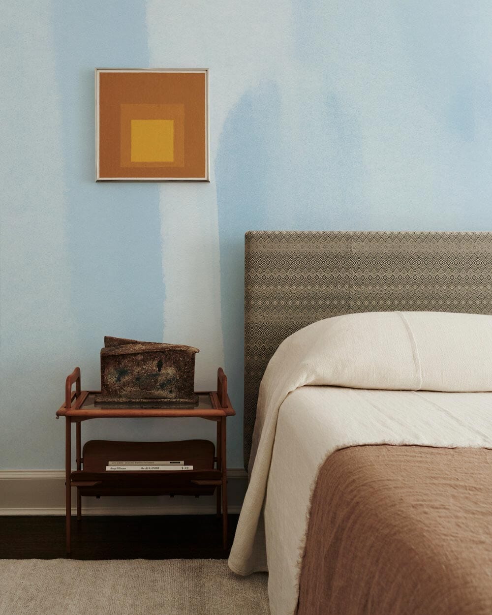 Bedroom featuring Sky Blue Watercolour Wallpaper, beige bed, modern artwork, hardwood flooring, minimalist decor.