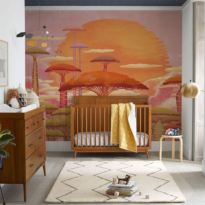 Sunset Glow Fantasy Trees Mural in nursery with wooden crib, dresser, and geometric rug on light flooring.