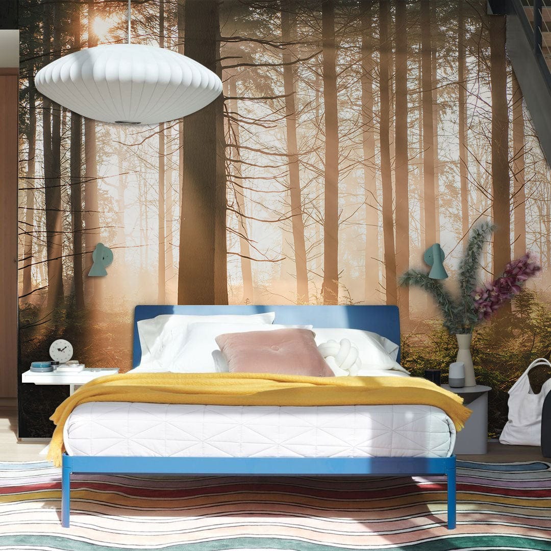 Serene Sunset Forest Mural Wallpaper in bedroom, featuring blue bed frame, striped rug. Atmospheric decor.