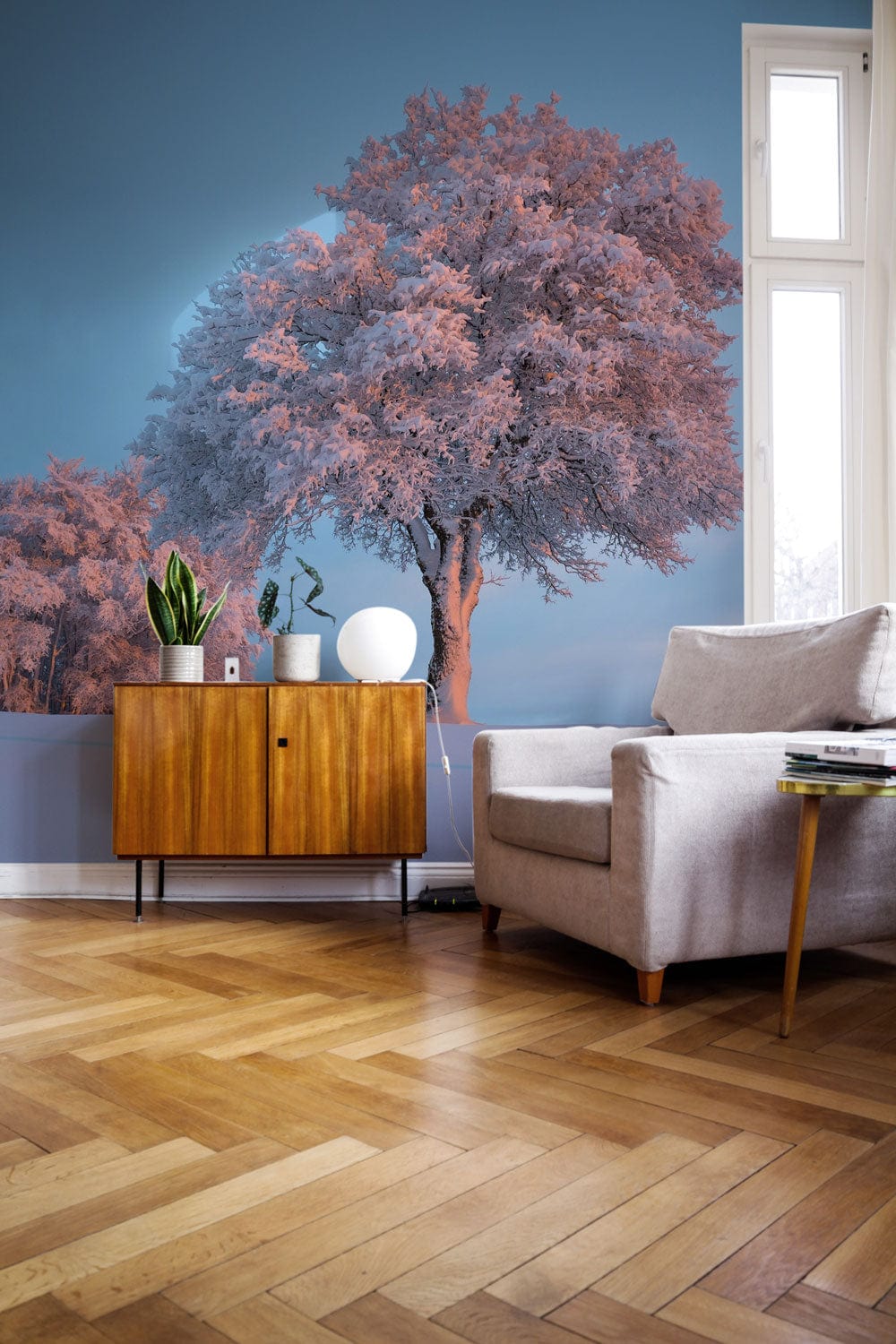 Elegant winter tree mural, soft blue, mid-century cabinet, grey sofa, herringbone flooring, living room.