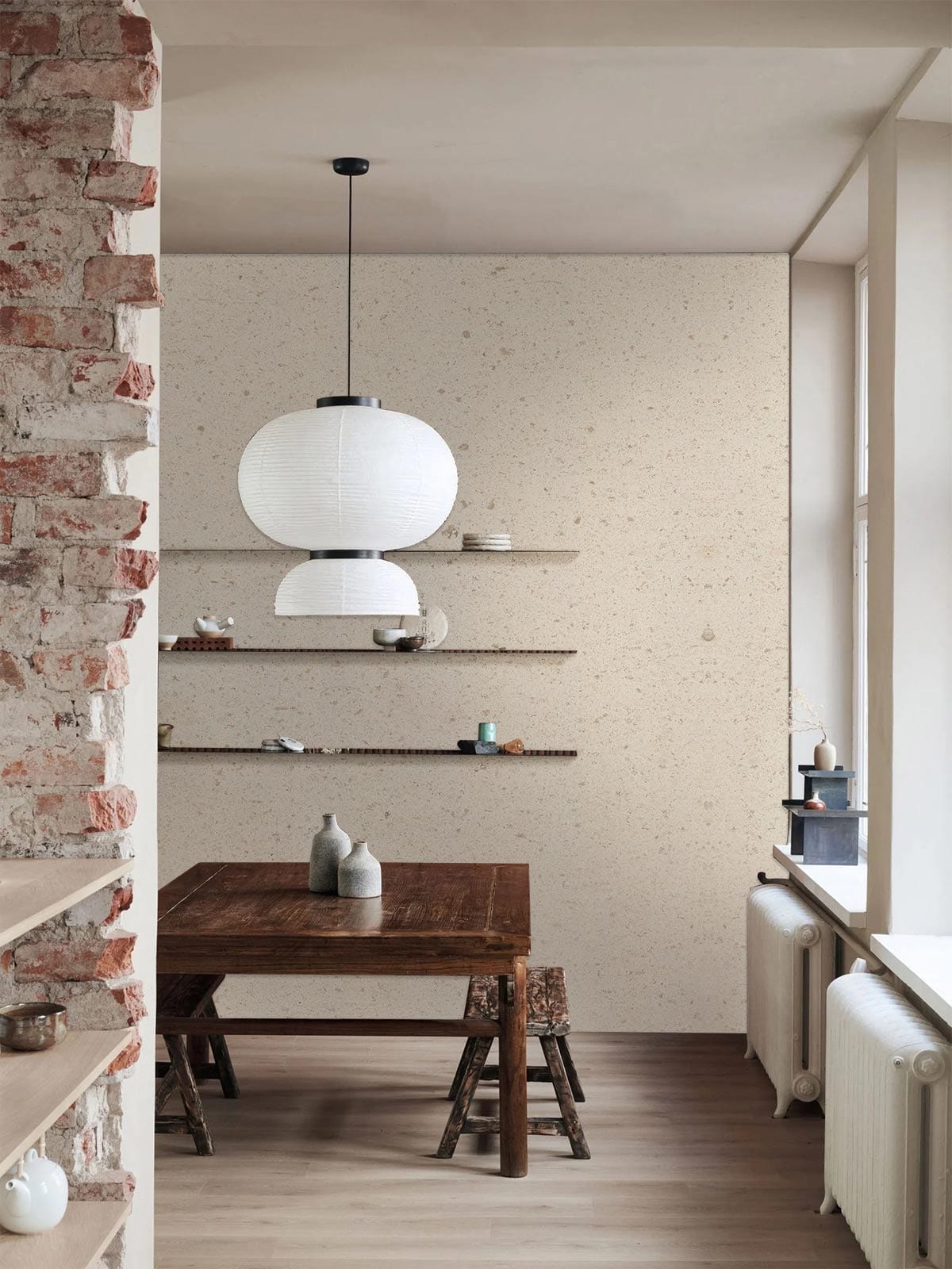 Elegant cream speckled wallpaper in minimalist dining room with wooden table, brick wall, hanging lamp.