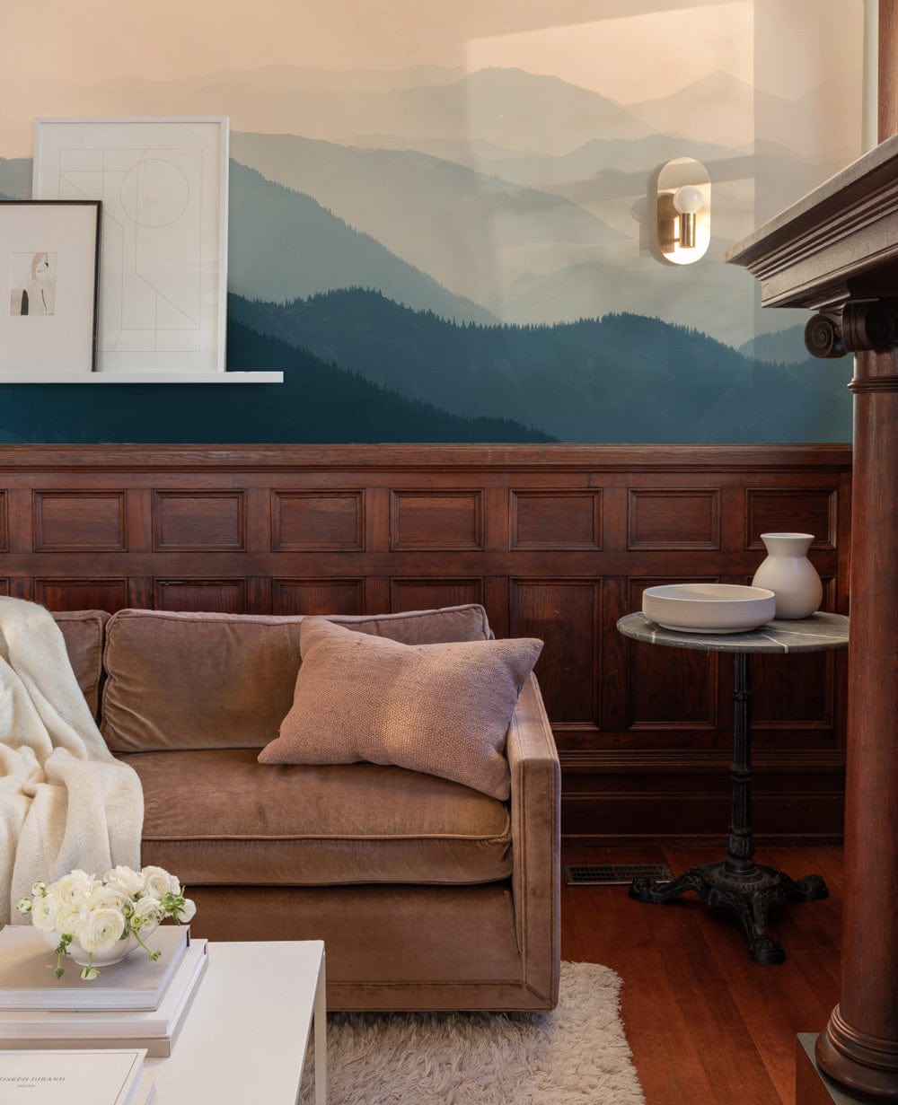 Serene Misty Mountain Range Mural with velvet sofa, wooden panelling, side table, and wall sconce.