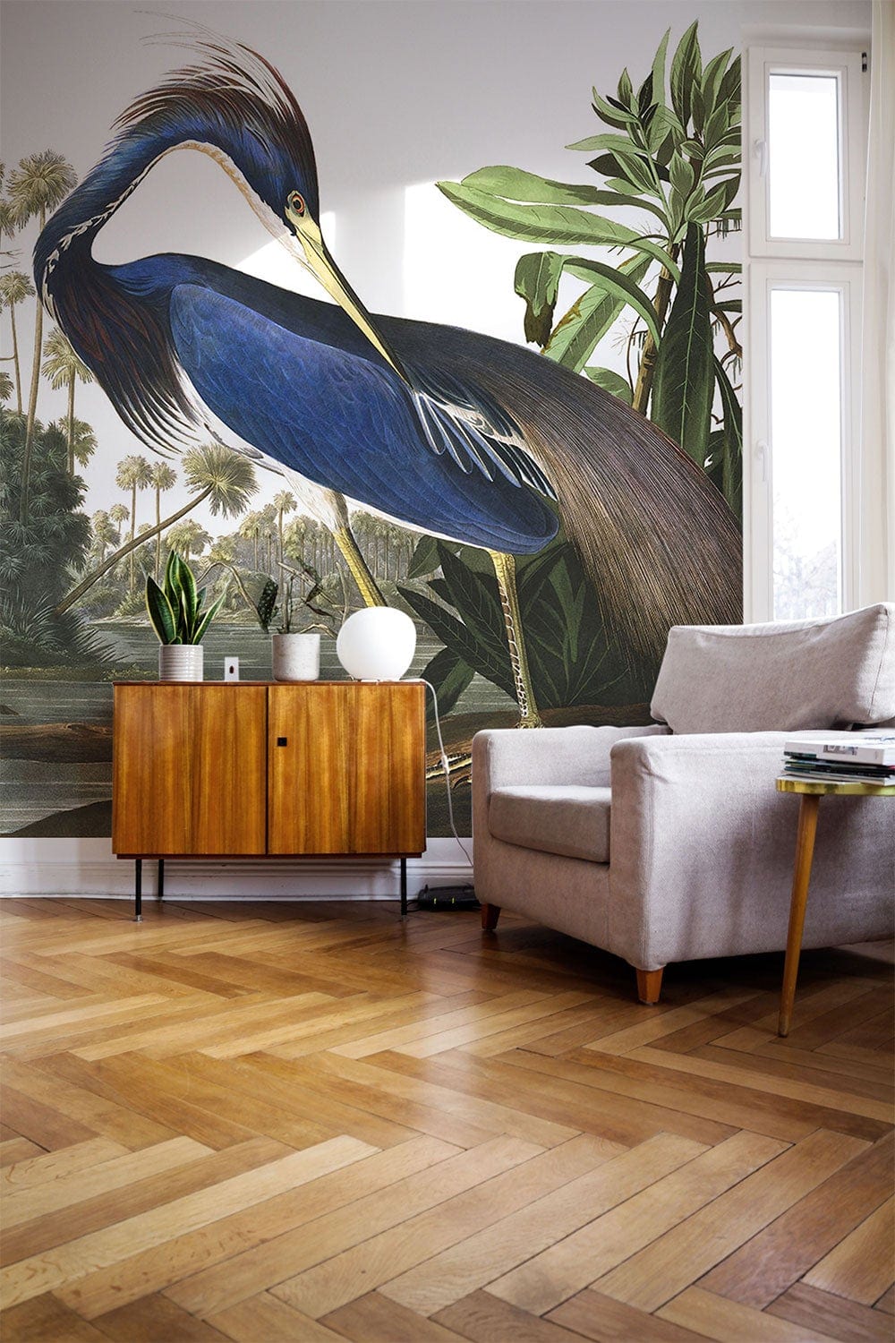 Elegant Blue Heron Tropical Nature Mural Wallpaper in modern living room with grey sofa and wooden flooring.