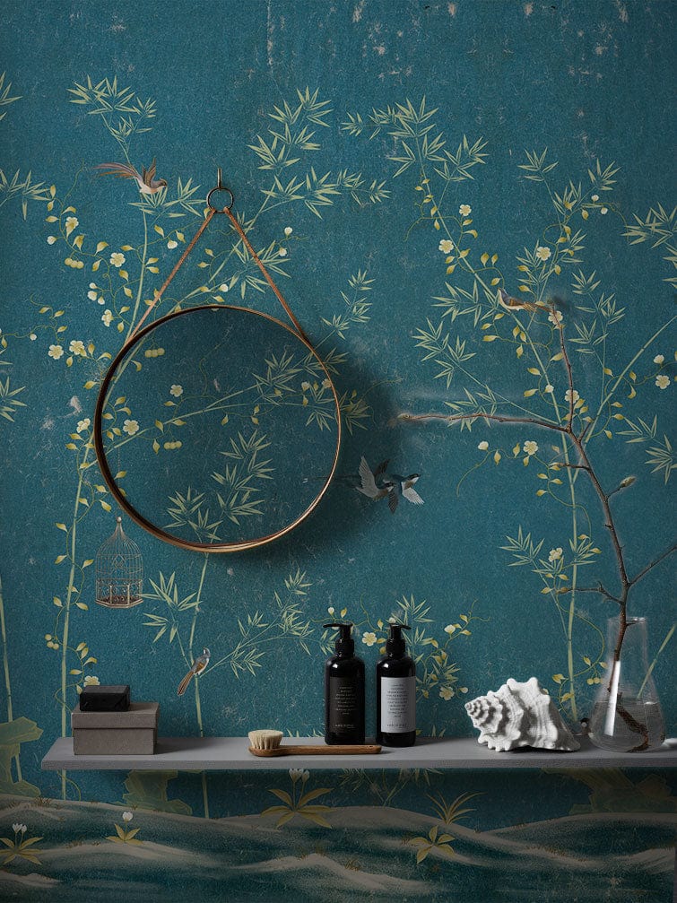 Elegant teal chinoiserie wallpaper featuring birds, florals, round mirror, shelf, bottles, and art decor.