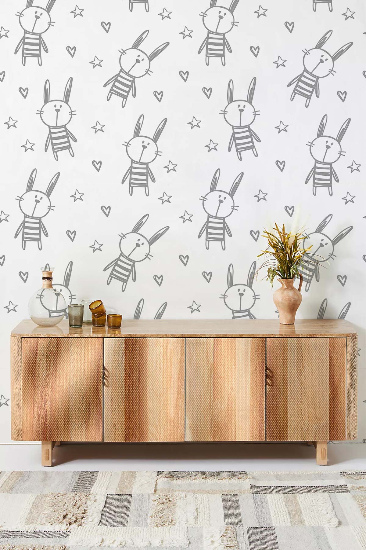 Cute grey bunny and star nursery wallpaper with light wood cabinet, geometric rug, and chic accessories.