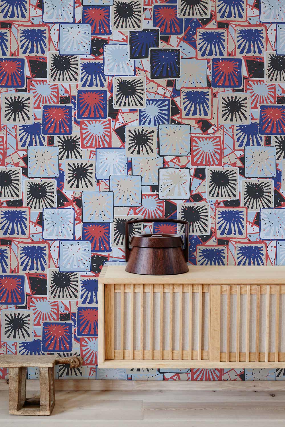 Retro geometric tile patterned wallpaper, red-blue-black design, wood console and stool in living room.