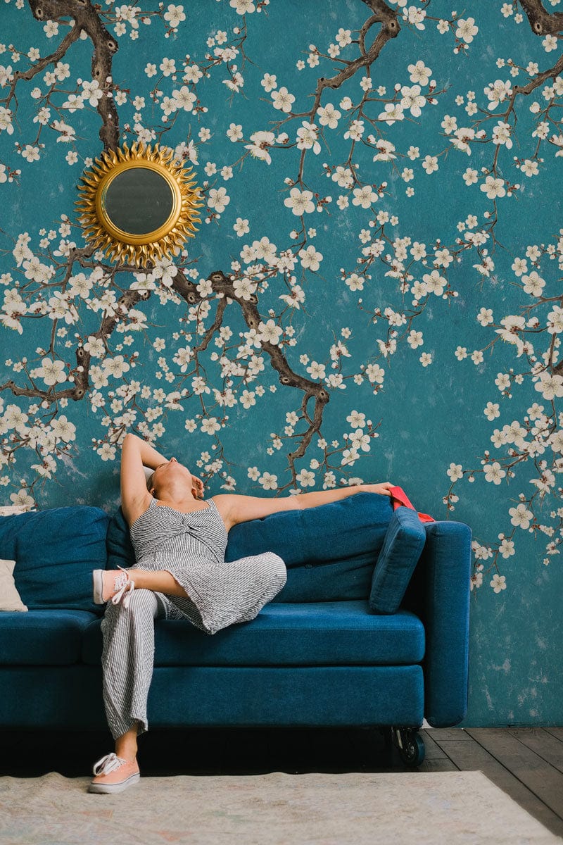 Teal Blossom Branches floral wallpaper, blue sofa, mirror, wood flooring, elegant living room decor.
