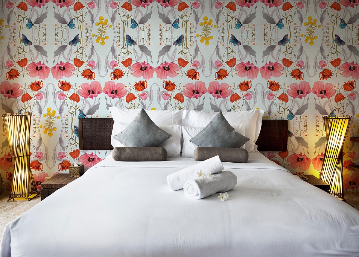 Bedroom with Floral Harmony mural wallpaper, featuring vibrant pastel hues, white bedding, and wicker lamps.