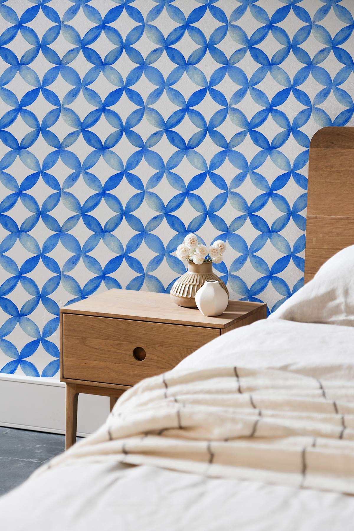 Blue geometric wallpaper with wooden bedside table and beige bedding in a modern bedroom setting.