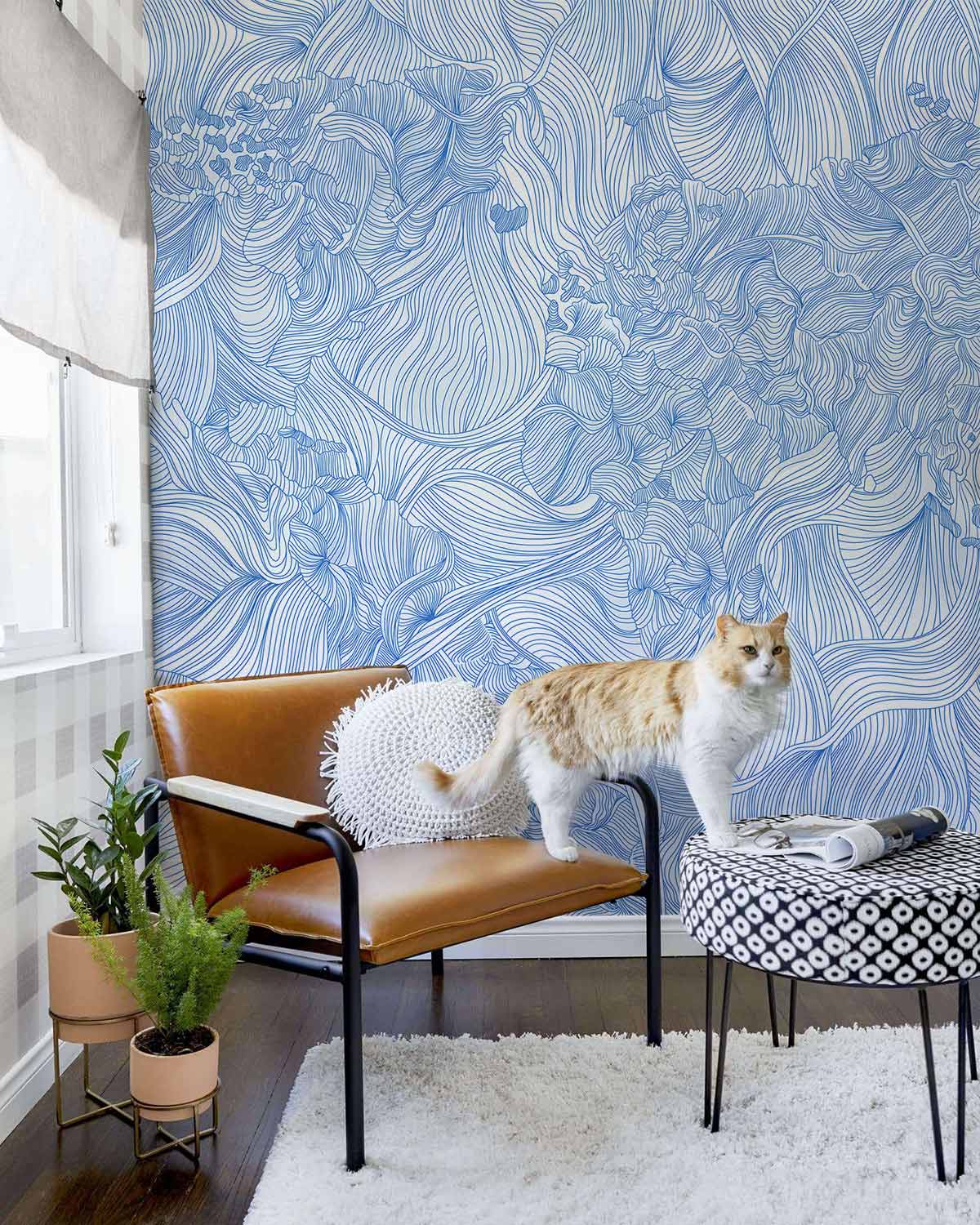 Elegant Blue Floral Line Art Wallpaper in living room with brown chair, cat, and geometric ottoman.