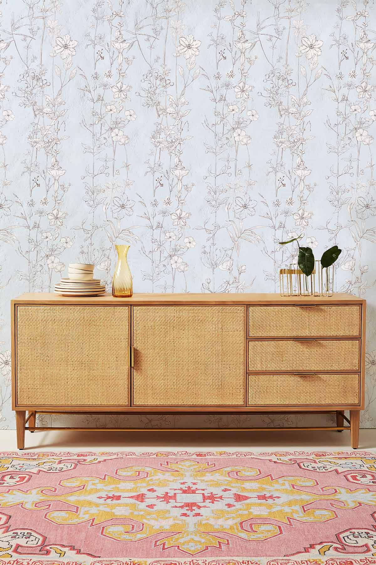 Elegant floral wallpaper with botanical design behind wooden cabinet, colourful rug, sophisticated room setting.