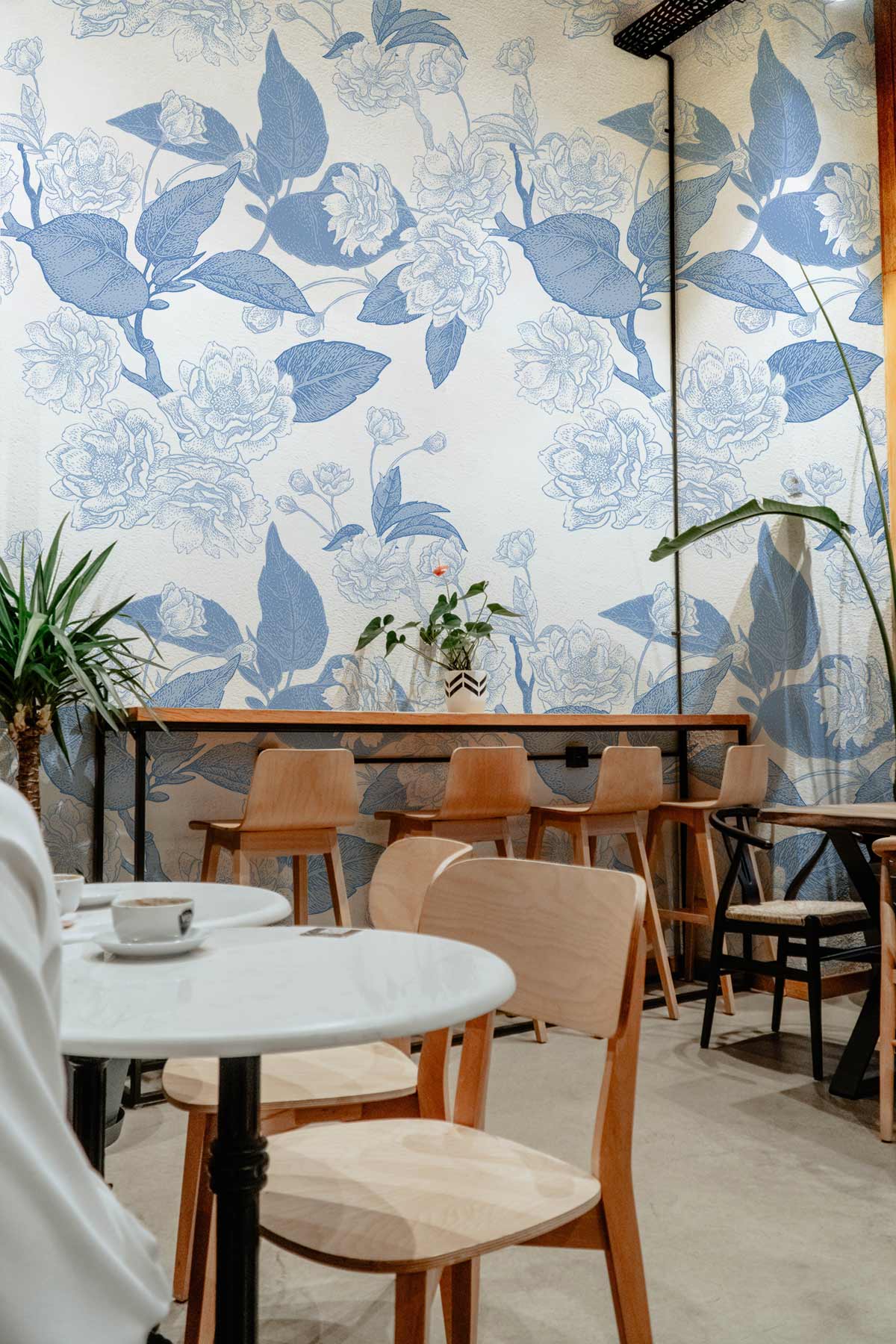 Vintage blue floral wallpaper in elegant café with wooden chairs, marble tables, and concrete flooring.
