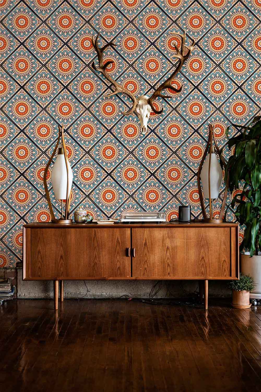 Moroccan geometric blue-orange boho tile wallpaper, wooden sideboard, dual mirrors, hardwood flooring, decorative antlers.