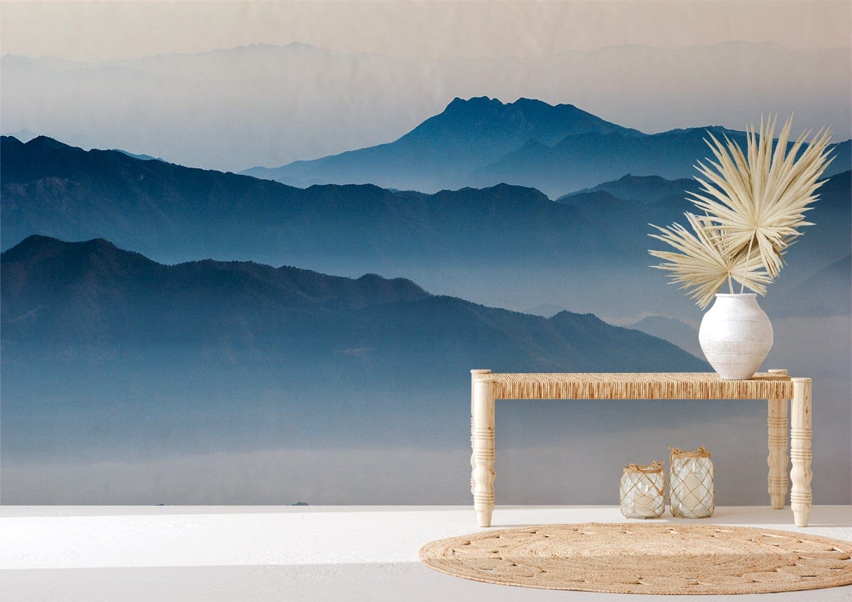 Tranquil Blue Mountain Mist Mural Wallpaper, light wooden table, wicker rug, white vase, serene interior.
