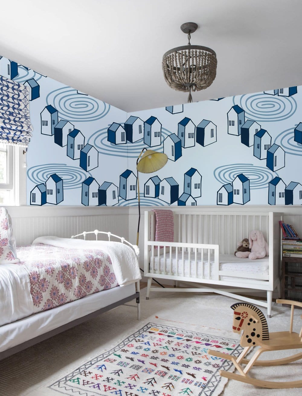 Charming blue geometric houses wallpaper, modern nursery with cot, white bed, and chandelier lighting.