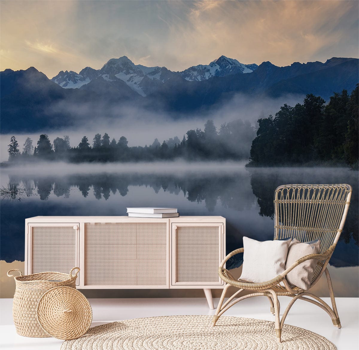 Tranquil mountain lake mural wallpaper with wicker chair, beige cabinet, and round jute rug in lounge.