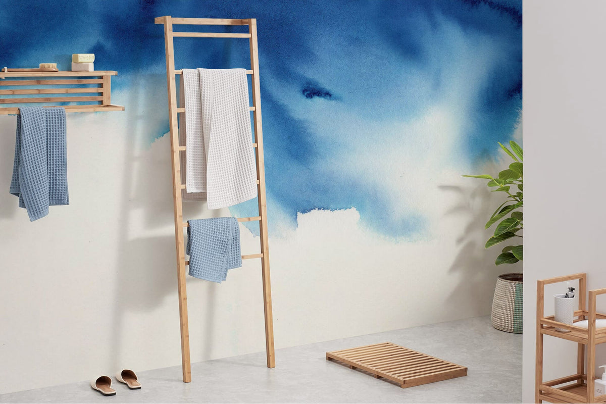 Elegant Blue Watercolour Sky Mural Wallpaper in bathroom with bamboo ladder, blue towels, grey floor.