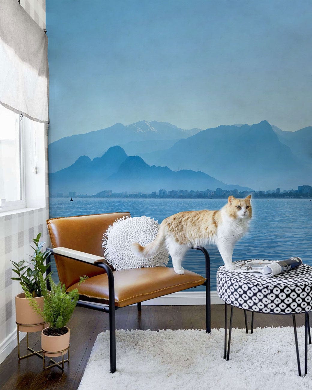 Tranquil Blue Mountain Wallpaper, tan armchair, geometric ottoman, in modern living room. Wall dimension available.