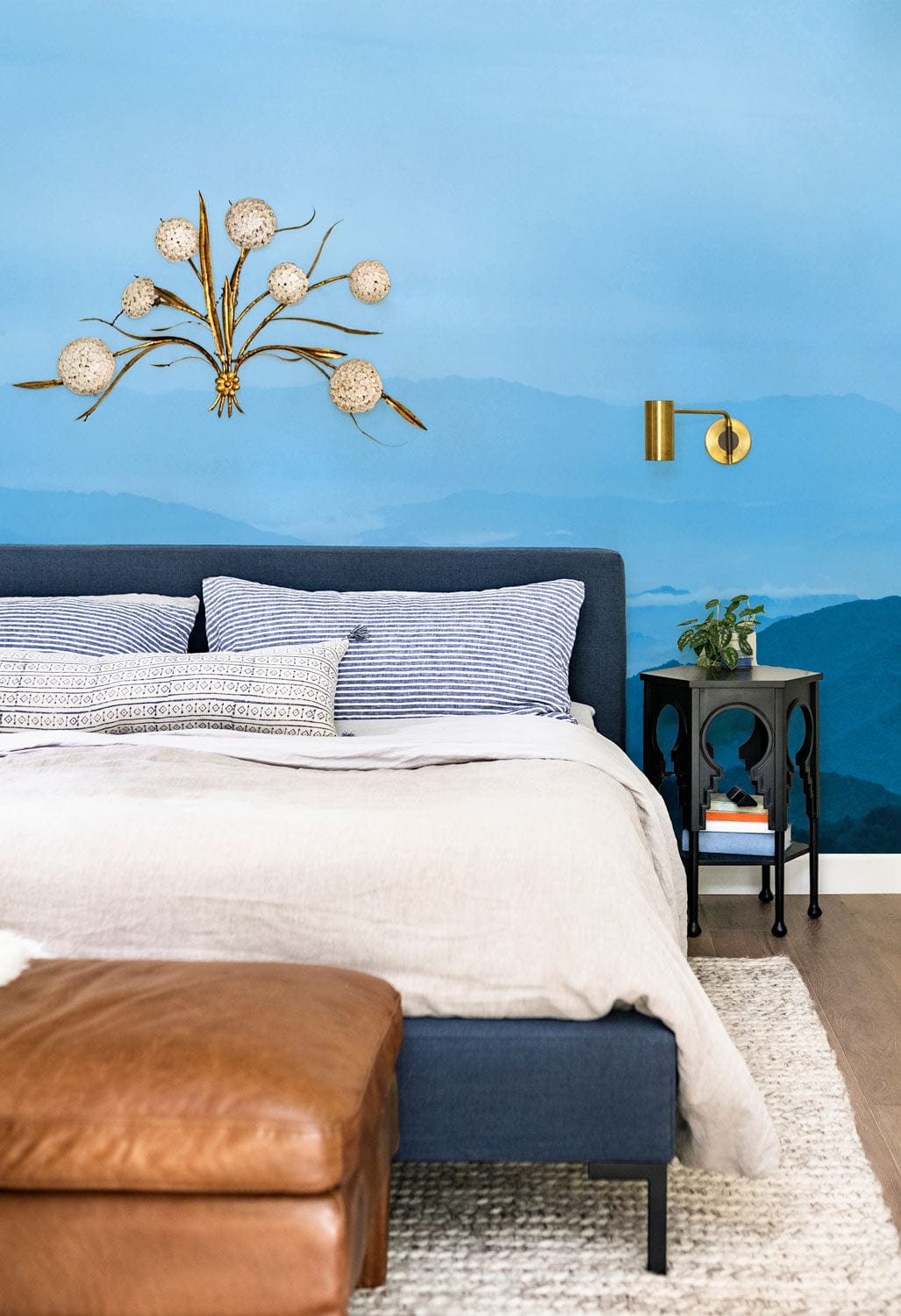 Blue Mountain Mist Mural Wallpaper in bedroom with blue bed, leather ottoman, and stylish lighting.