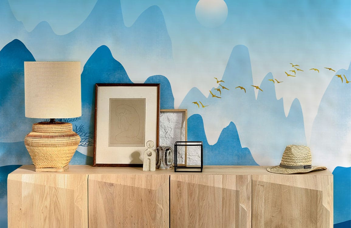 Serene blue mountain mural wallpaper enhances room with wooden sideboard, wicker lamp, straw hat Décor.