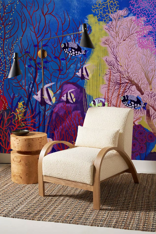 Tropical underwater mural wallpaper in vibrant blue, armchair, wooden side table, woven rug, modern decor.