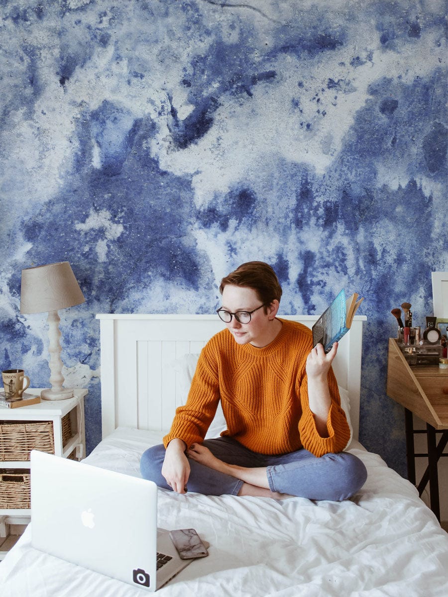 Blue abstract watercolour mural wallpaper, white bed, orange jumper, rustic desk, cosy bedroom design.