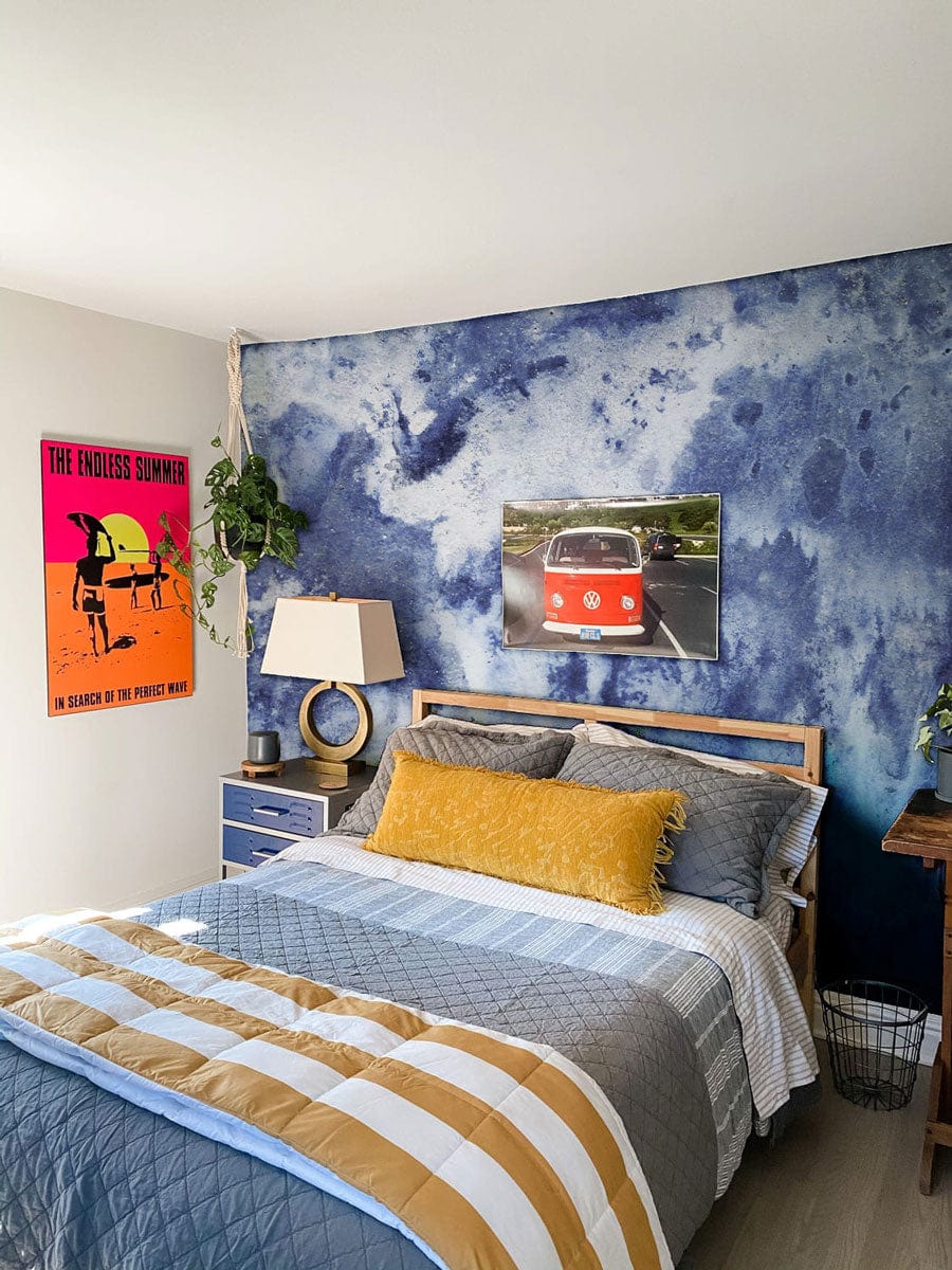 Blue Abstract Watercolour Texture Mural Wallpaper in bedroom, wooden bed, striped bedding, light flooring.
