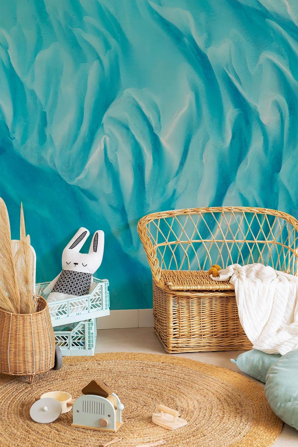 Aqua Coastal Dreamscape Mural Wallpaper with wicker chair, blue accents, round jute rug, in nursery.