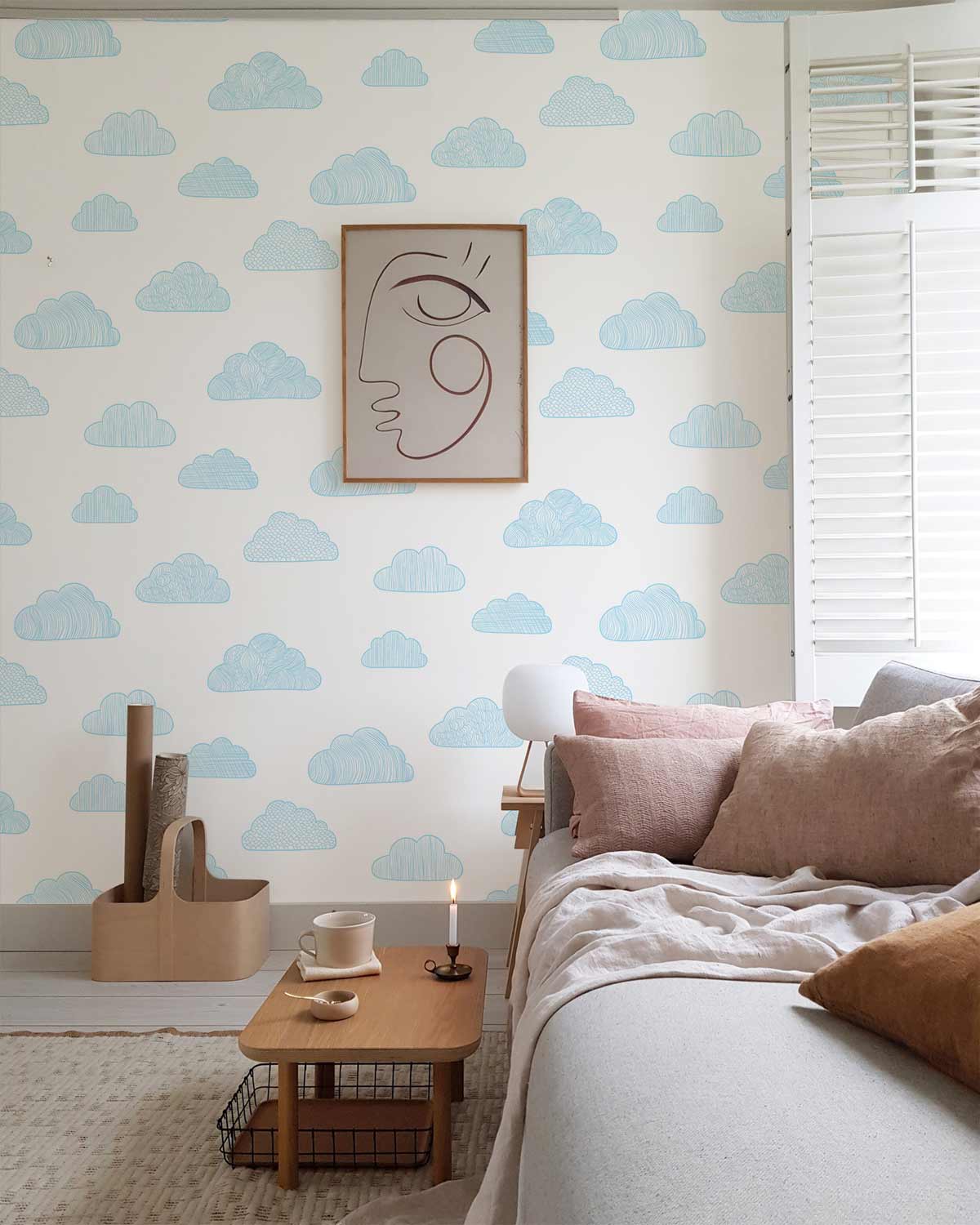 Dreamy blue cloud wallpaper in nursery, neutral sofa, wooden table, beige throw, minimal wall art.