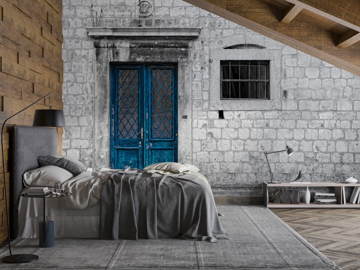 Vintage stone wall mural in bedroom with grey bed, wooden flooring, and distressed blue door charm.