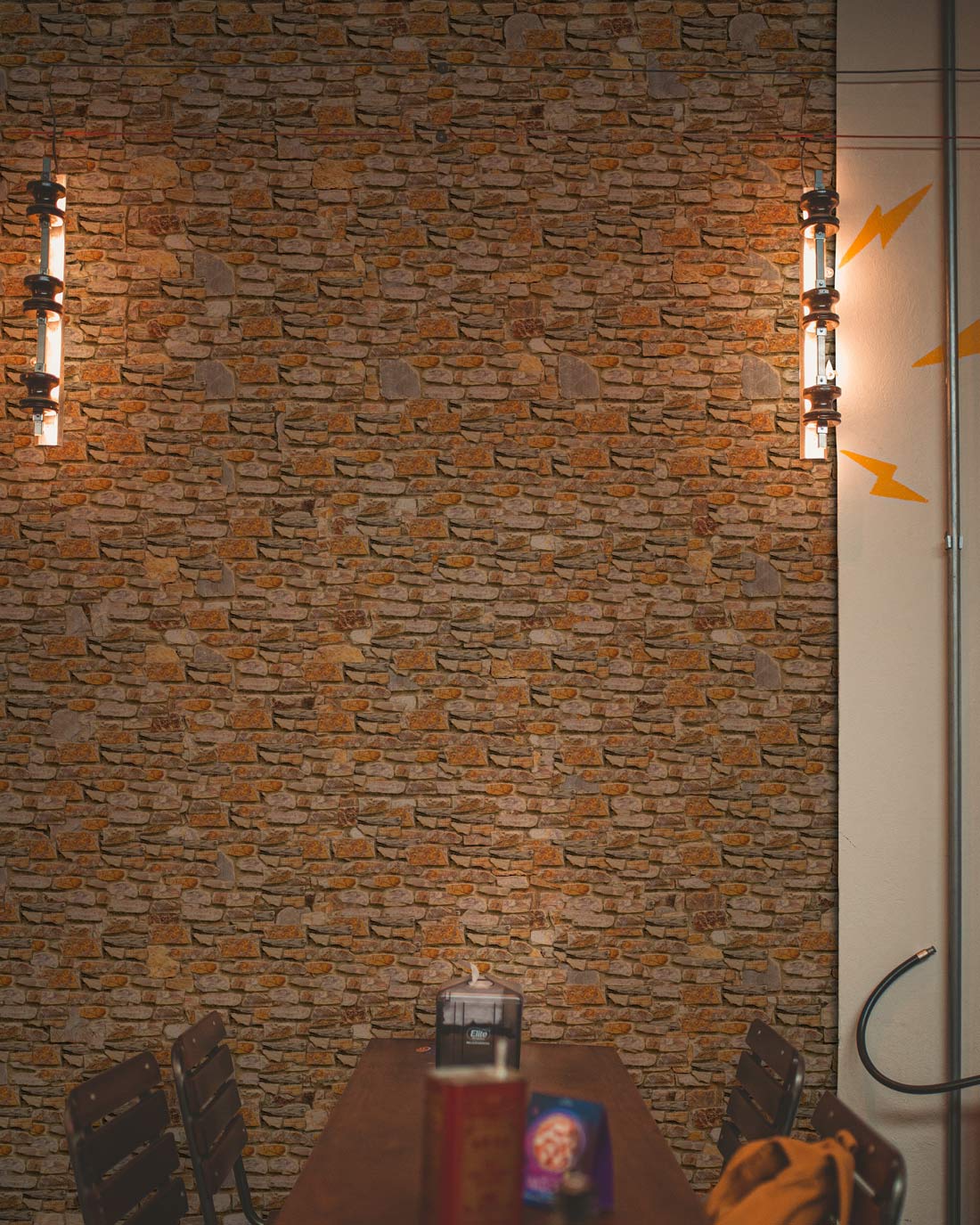 Rustic stone wallpaper with natural tones, complemented by industrial lights and wooden dining table.