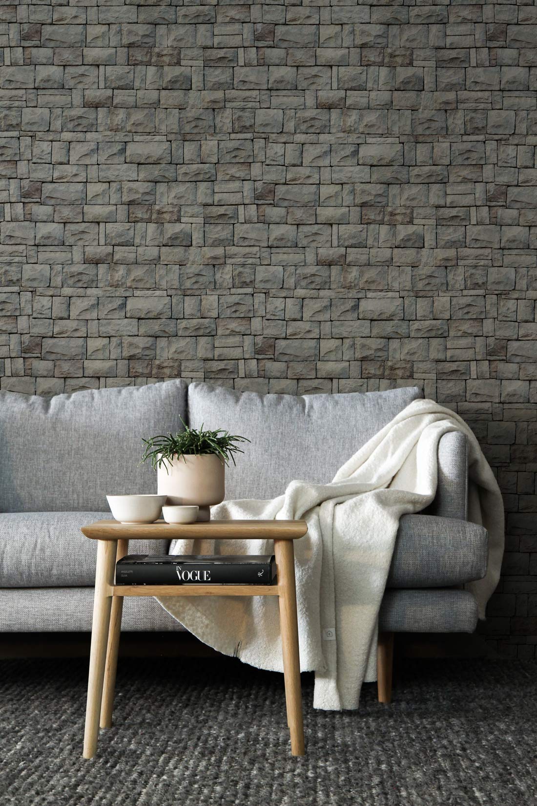 Rustic grey stone wallpaper, modern grey sofa, wooden coffee table, textured rug in living room.