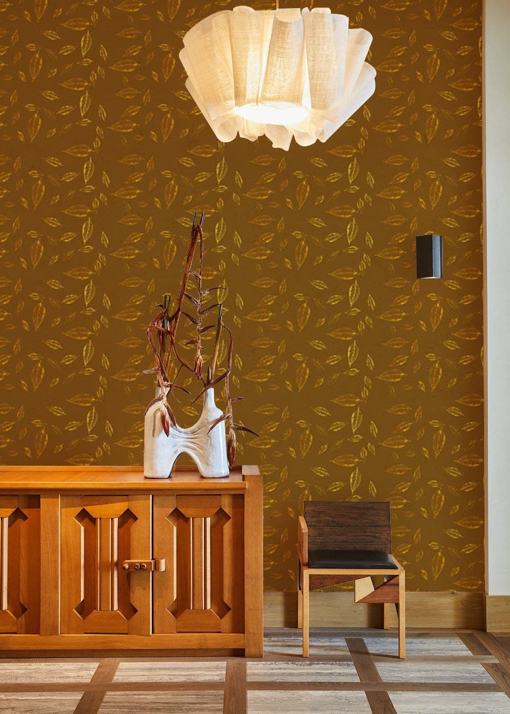 Elegant brown and mustard leaf wallpaper, wooden cabinet, minimalist chair, modern lighting, patterned flooring.