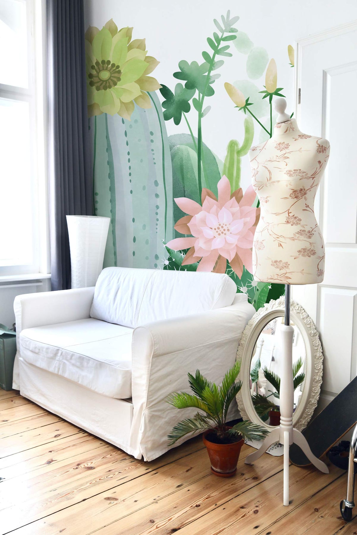 White sofa, mannequin, potted plant, and Watercolour Cactus Garden Mural Wallpaper in stylish living room.