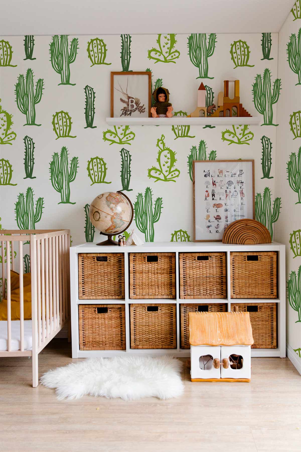 Green Cacti Patterned Wallpaper in nursery; wicker storage, white crib, light wood flooring, playful decor.