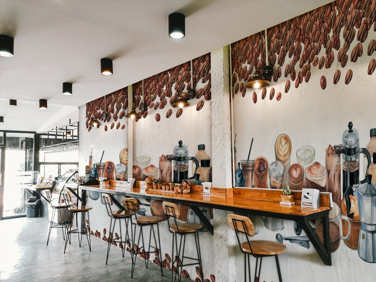 Cafe with coffee-themed mural, wooden bar stools, stylish hanging lights, and concrete flooring.