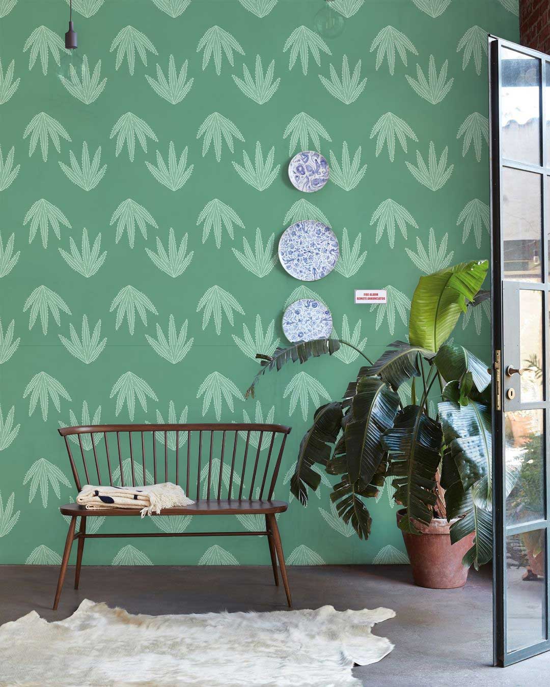 Elegant sage green leaf patterned wallpaper in modern interior with wooden bench, potted plant, plates.