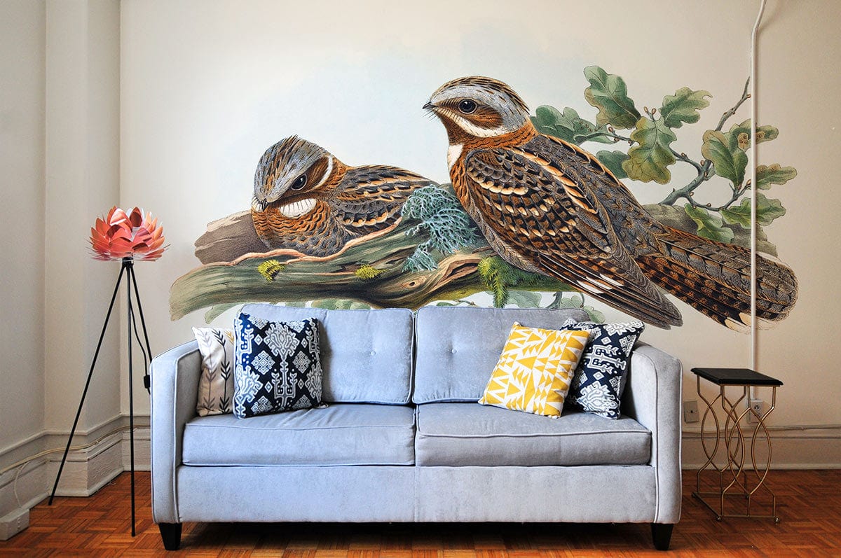 Vintage bird wallpaper with earthy tones behind light grey sofa, wooden flooring, and tripod floor lamp.