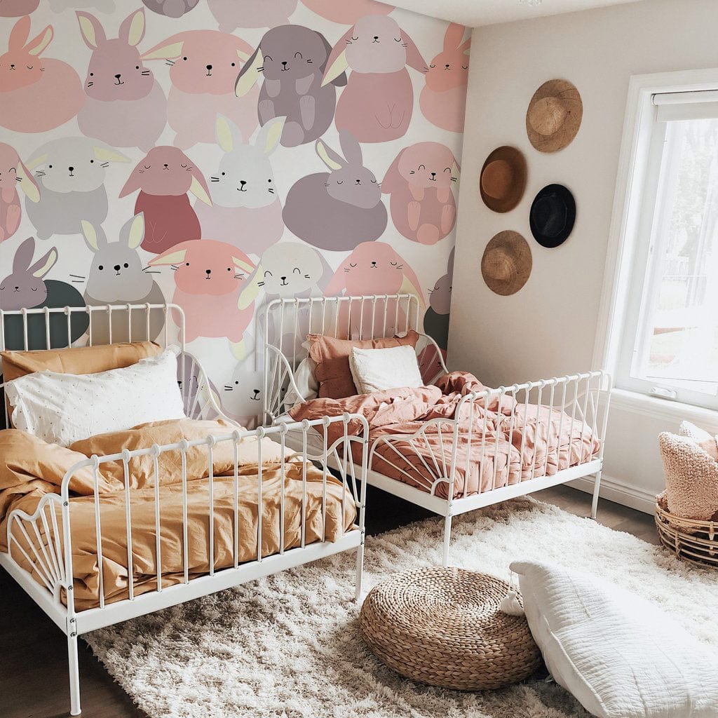 Playful pastel bunny mural wallpaper in nursery with white beds, shaggy rug, and woven wall decor.
